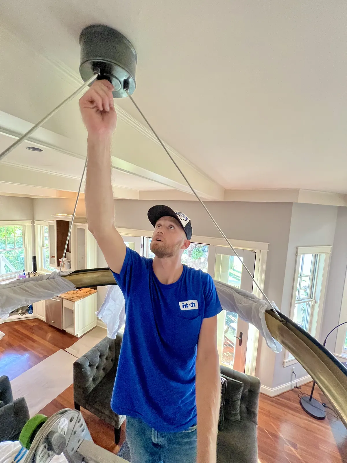 Intech electrician hanging a modern light fixture in a living room